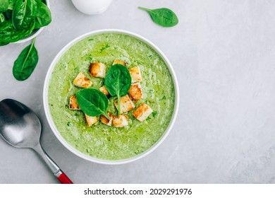 Green Cream Soup. Spinach broccoli creamy soup with croutons on gray stone background. Top view with copy space.