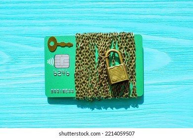 Green Credit Card Wrapped With A Chain And Secured With A Small Padlock Isolated On A Blue Wooden Background. Financial Safety And Fraud Protection Concept.