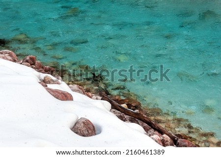 Green Cristal River Water with contrast of Snow on Riverbank Background