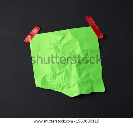 green crumpled sheet of paper glued with rubber red adhesive tape on a black background, copy space
