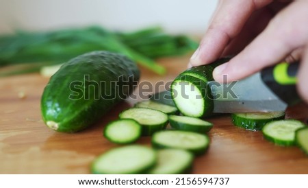 green cucumbers are cut with a knife in the kitchen. healthy food salad vegetables concept. close-up green cucumbers in the kitchen hands close-up cut into slices lifestyle