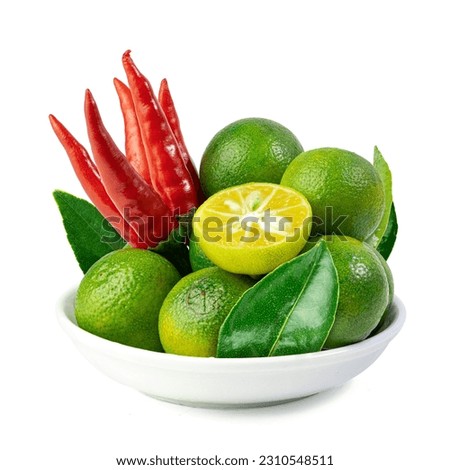 Green Cumquat or Kumquat fruits with leaves and red chilli peppers in a ceramic bowl isolated on a white background