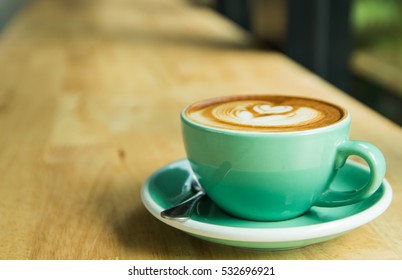 Green cup of latte art coffee on wooden table - Shutterstock ID 532696921