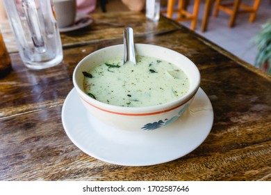 Green Curry Dish Served In Thai Restaurant In Thailand. Street Food Bowl Of Spicy Soup. Foodie Travel Background. Asian Food Experience. Simple Single Object On Wooden Table.