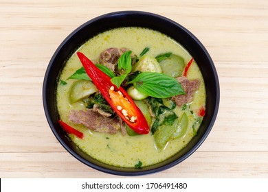Green curry, Thai green curry with beef chilli and eggplant ganished with slice fresh chilli and Basil leaf in black colour bowl on timber background.