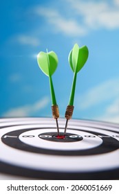 Green darts in center of dartboard over sky