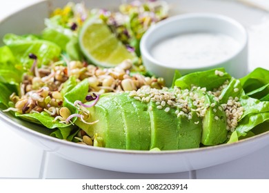 Green detox salad with avocado, sprouts, hemp seeds and yogurt dressing, white tile background, close-up.