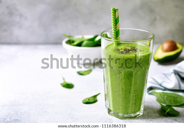 Green\
detox smoothie from avocado and baby spinach in a tall glass on a\
light grey slate, stone or concrete\
background.