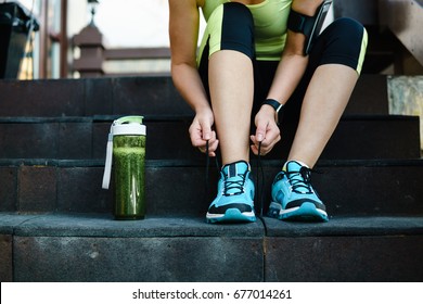 Green detox smoothie cup and woman lacing running shoes before workout. Fitness and healthy lifestyle concept.