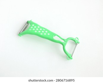 Green double sided plastic vegetable peeler with textured ergonomic handle and dual blades placed diagonally on minimal clean light surface with copyspace