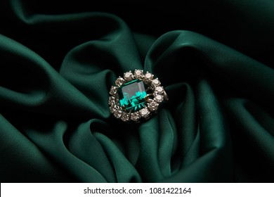 Green Emerald Fashion Engagement Diamond Ring On Green Satin Background. Luxury Female Jewellery, Close-up. Selective Focus