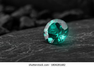 Green emerald oriental sapphire gemstone with dark rock background.