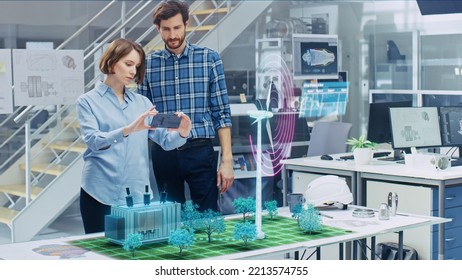 Green Energy Concept: Two Eco-Engineers Use Augmented Reality Smartphone to Design 3D Wind Turbine Park Hologram on the Table. Generating Sustainable and Renewable Clean Power for Society. - Powered by Shutterstock