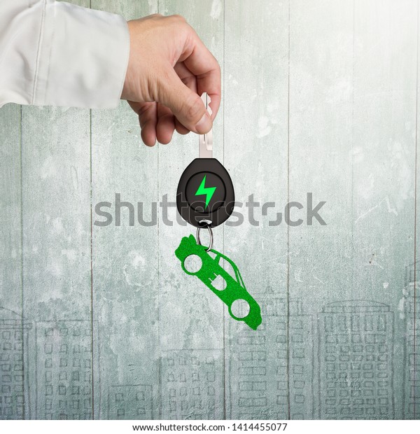 Green energy electric car and Eco-friendly
environmental protection concept. Man hand holding electric car key
with green leaves keyring in sports car shape, on doodels wall
background.