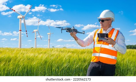 Green Energy. Man With Drone. Wind Energy Company Employee. Windmills In Green Field. Man Is Employee Of Energy Company. Concept Surveying Wind Turbines With Drone. Guy In Helmet Launches Quadcopter