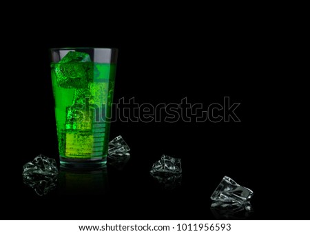 Green energy soda drink glass with ice cubes on black background
