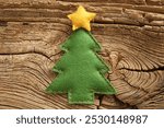 A green felt Christmas tree decoration with a yellow star on top, placed on a rustic wooden background