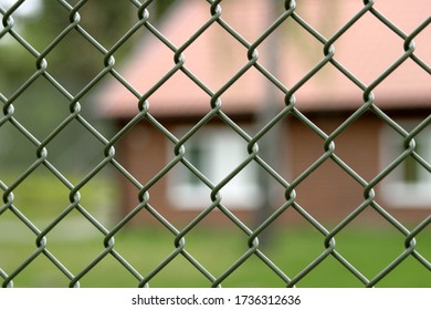 A Green Fence In Focus With A Red Building In The Background. Taken At A Youth Detention Center In Stockholm. The Fence Is Ment So Symbolize Incarceration.