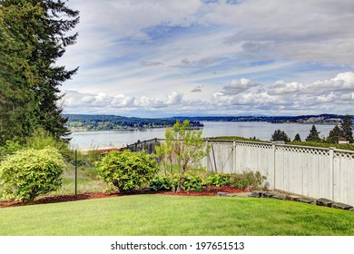 Green Fenced Backyard With Bushes, Lawn And Water View