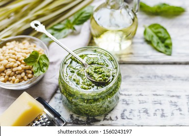 Green fettuccine and Pesto sauce in vintage spoon on glass jar of pesto sauce with ingredients on rustic white wooden table. Traditional Italian pesto recipe for making fettuccine, pasta, bruschetta.