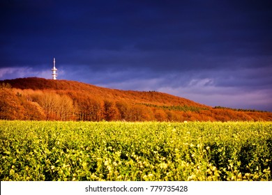 Green field and distant hills in golden light after a storm under a dark blue brooding sky with a tower in a scenic landscape - Powered by Shutterstock