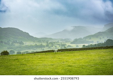 Green fields, stone wall, and misty mountains in the Lake District National Park. Rural Cumbria, England.
