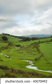 Green fields with stream running through on a cloudy day