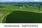 Green fields stretch out endlessly, featuring rows of crops interspersed with farm buildings under a cloudy sky. The landscape shows the beauty of rural life in the countryside.