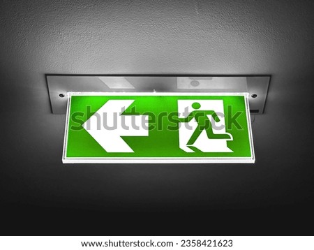 A green fire exit sign is placed on the ceiling along the dimly lit corridor.