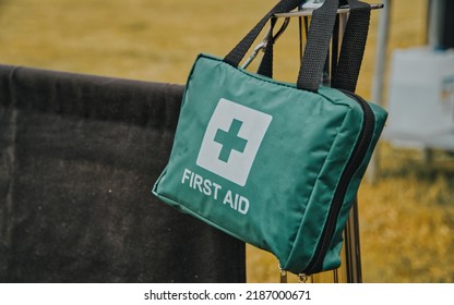 Green First Aid Bag With Black Straps Hanging On A Silver Metal Pole On A Summers Day At A Barbeque