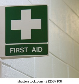 Green First Aid Sign Mounted To Wall On White Background.