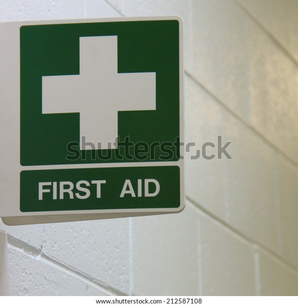 Green\
First Aid sign mounted to wall on white\
background.