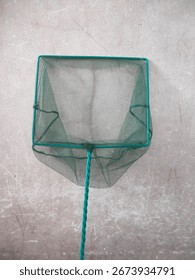 Green fish net with a square frame and twisted handle, ideal for catching small fish or aquarium maintenance, shown against a plain textured wall