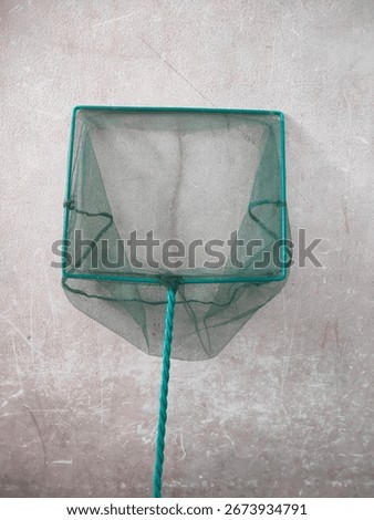 Green fish net with a square frame and twisted handle, ideal for catching small fish or aquarium maintenance, shown against a plain textured wall