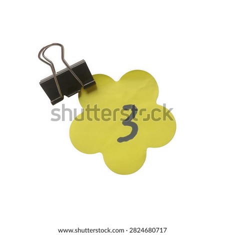 Green flower shape note with number three clipped by a black binder clip isolated on white background
