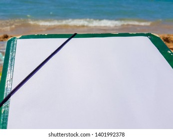 Green folder with a white leaf on the beach. Image to accompany studies and holidays