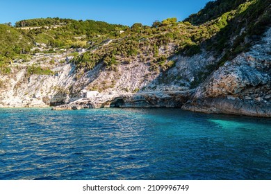 Green forest-covered high rocky steep cliffs on shore of Grecian Corfu island with clear blue sea water under cloudless sky panorama view