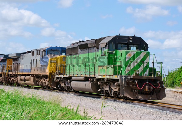 Green freight train pulling a blue and yellow
train as they speed down the
track