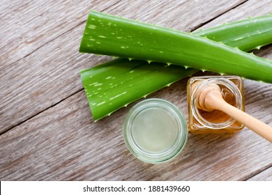 Green fresh aloe vera leaf with aloe gel and pure honey in glass jar isolated on wood table background.