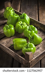 Green fresh shiny bell peppers front view vertical colorful arrangement in old brown wooden box and dark background in studio