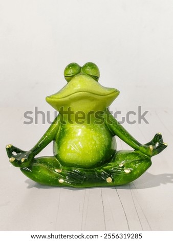 A green frog is sitting in a pose that looks like it is meditating. The frog is sitting on a white surface, and it is in a peaceful and calm state