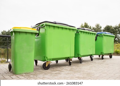 Green garbage containers in a row on stony street