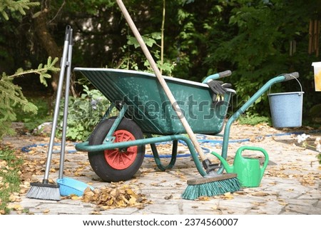 Green garden wheel with broom, leaves, bucket, gloves and garden hose.