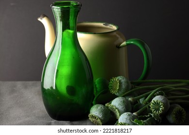 GREEN GLASS VASE AND CREAM COLORED ENAMEL CAN WITH GREEN POPPY SEED PODS ON STEMS