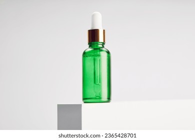 Green glass vial with gold dropper cap is on platform. - Shutterstock ID 2365428701