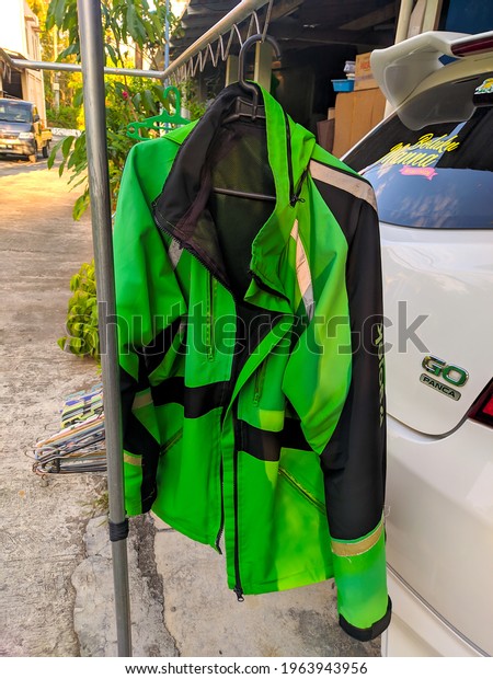 A green Gojek jacket is drying on a cloth drying in\
the morning behind a white car. Yogyakarta, Indonesia - April 28,\
2021.