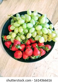 Green grapes and red strawberries on black plate