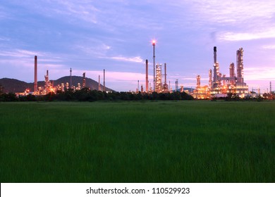 Green Grass Field With Scenic Of Petrochemical Oil Refinery Plant Shines At Night