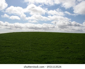 Green Grass On A Hill Slope On The Background Of Blue Sky With Clouds Similar To An Old PC Windows Desktop Wallpaper