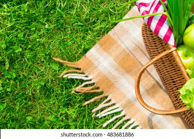 Green grass and straw basket with food on checkered beige tablecloth background for picnic, top view